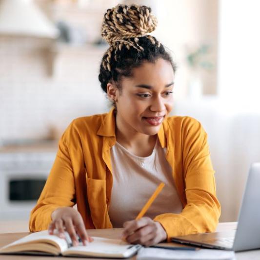 Student studying remotely from home with a book open.