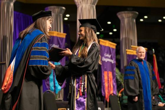 Dr. Candice McQueen handing a graduate her diploma.